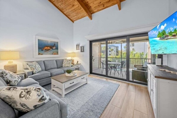 Un soggiorno moderno con divano, tavolino e televisione, affacciato su un balcone con vista sul mare.