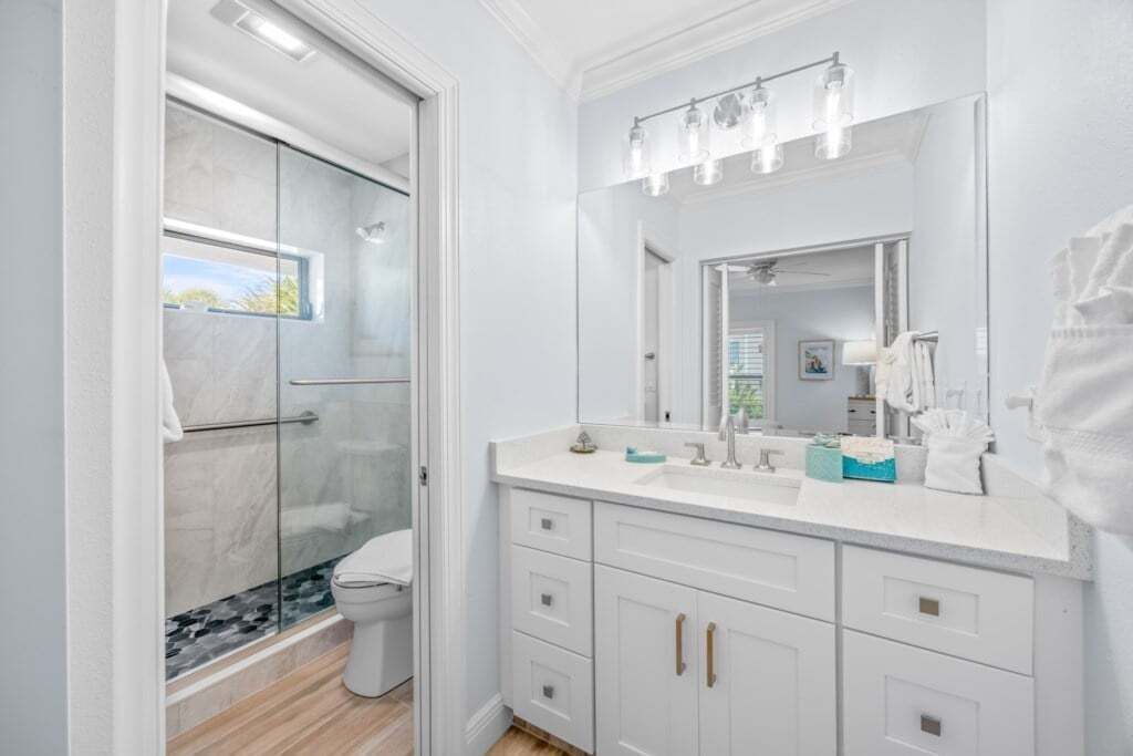 Une salle de bain moderne avec une douche à l’italienne en verre, un grand miroir et un meuble-lavabo blanc doté de tiroirs.