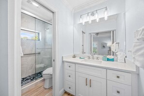 Un bagno moderno con cabina doccia in vetro, uno specchio grande e un mobile lavabo bianco con cassetti.