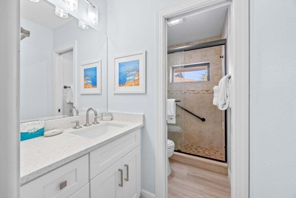 A modern bathroom with a large mirror, two framed pictures, a white sink, and a shower area.