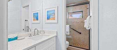 A modern bathroom with a large mirror, two framed pictures, a white sink, and a shower area.