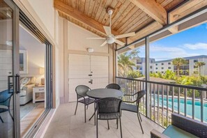 Un balcone con un tavolo rotondo e sedie, una ventola a soffitto e vista su una piscina e degli edifici.