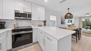 A modern kitchen with white cabinetry, stainless steel appliances, and a large island. - Seashells Unit 36 2 Bedroom Condo (Sanibel)