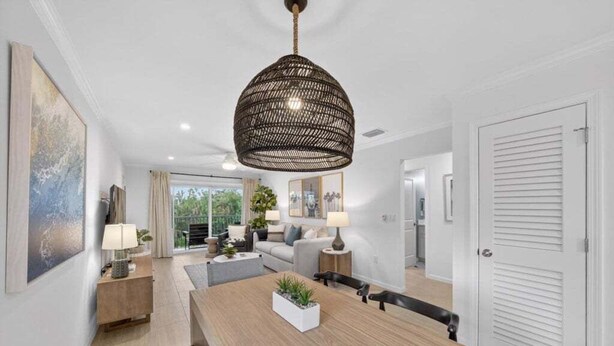 A modern living room with a wooden dining table, a large woven pendant light, and a view of the outdoors. - Seashells Unit 36 2 Bedroom Condo (Sanibel)
