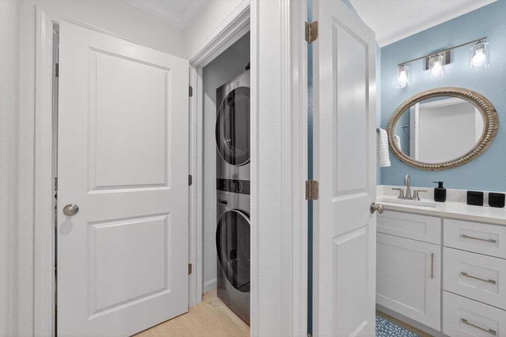 Een badkamer met een witte deur, een blauwe muur, een ronde spiegel, een wastafel en een wasmachine.
