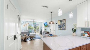 A modern kitchen with a marble countertop, pendant lights, and a view to the living area. - Seashells Unit 37 2 Bedroom Condo (Sanibel)
