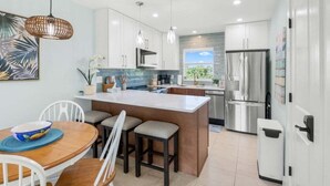 A modern kitchen with white cabinets, a large island, stainless steel appliances, and pendant lighting. - Seashells Unit 37 2 Bedroom Condo (Sanibel)