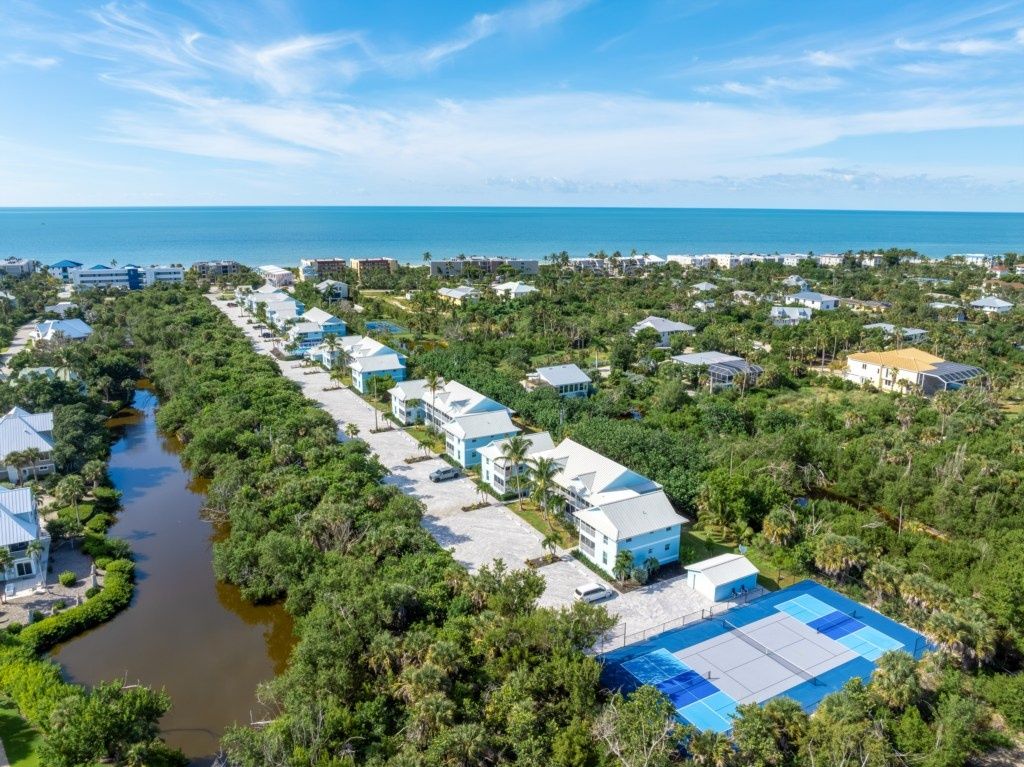 A coastal residential area with houses along a river, a clear sky, and the ocean in the distance.