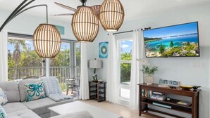 A modern living room with a large sofa, a TV, and a balcony with a view of the sea. - Seashells Unit 37 2 Bedroom Condo (Sanibel)