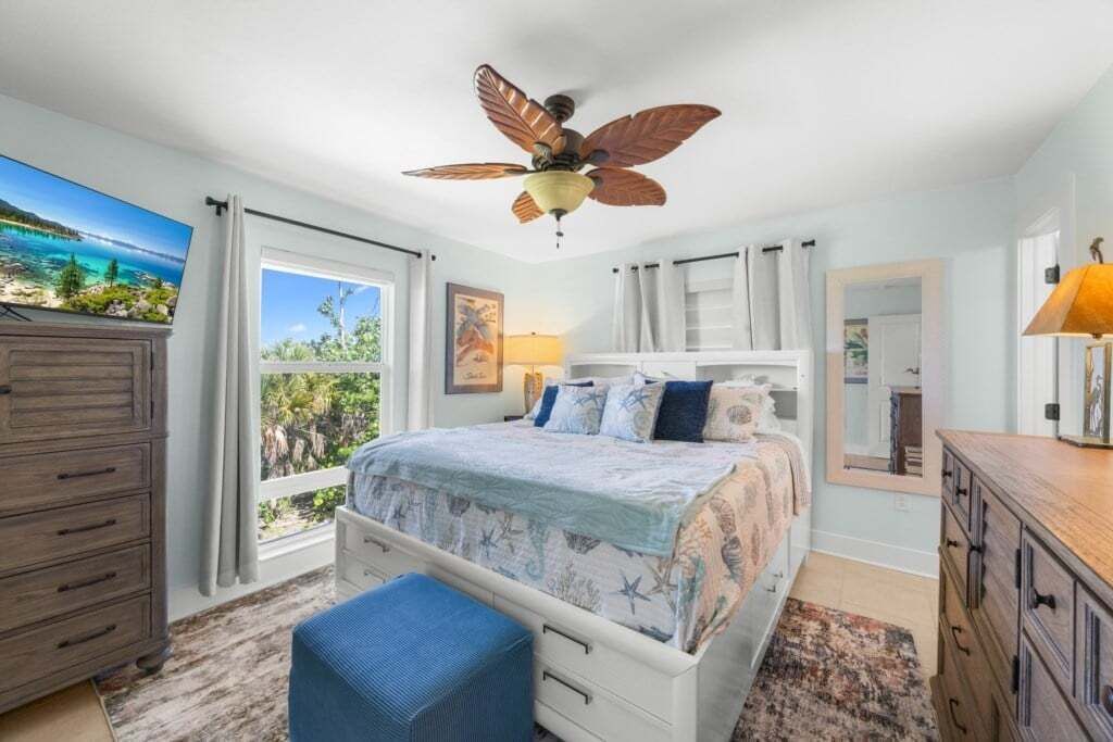 Une chambre à coucher comprenant un lit, un ventilateur de plafond, une commode, une fenêtre avec des rideaux et une vue sur l’extérieur.