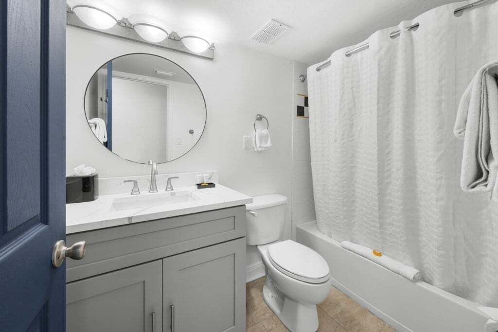 Une salle de bain avec des toilettes blanches, un lavabo avec un miroir au-dessus et un rideau de douche.