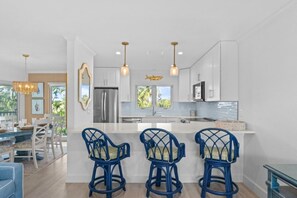 A modern kitchen with white cabinetry, a central island, and blue bar stools. - Seashells Unit 20 - Shiny Star 2 Bedroom Condo (Sanibel)