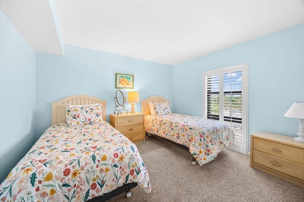 A bedroom with two beds, a nightstand, a dresser, and a window with blinds.
