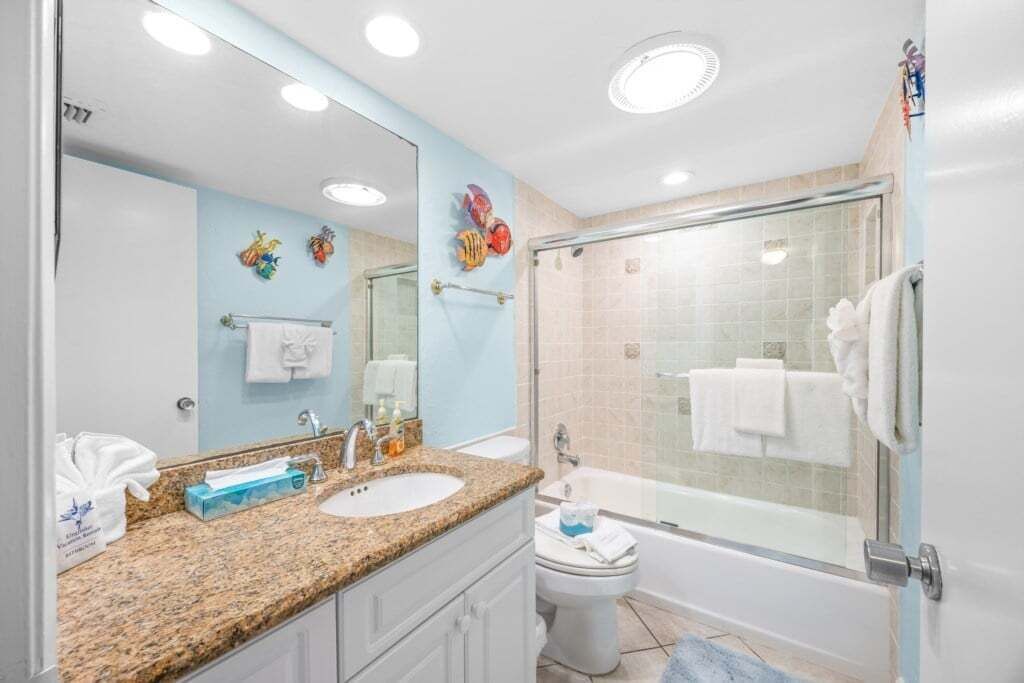A bathroom with a granite countertop, a sink, a mirror, a toilet, and a glass-enclosed shower.