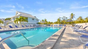 A swimming pool with lounge chairs and a building with a sloped roof. - Chic Island Haven - Seashells Unit #38 2 Bedroom Condo (Sanibel)