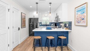 A modern kitchen with a large island, bar stools, pendant lighting, and a view of the outdoors. - Chic Island Haven - Seashells Unit #38 2 Bedroom Condo (Sanibel)