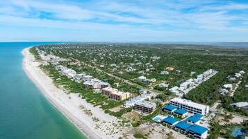 Vista aérea de un complejo turístico costero con propiedades frente a la playa, una playa y un denso grupo de edificios.