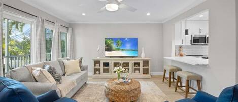 A modern living room with a sofa, ottoman, and a flat-screen TV on a cabinet.