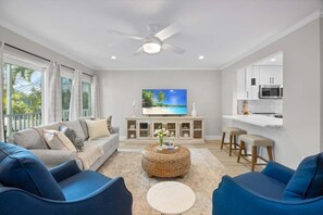 A modern living room with a sofa, ottoman, and a flat-screen TV on a cabinet. - Seashells Unit 18-coastal Breeze 2 Bedroom Condo (Sanibel)