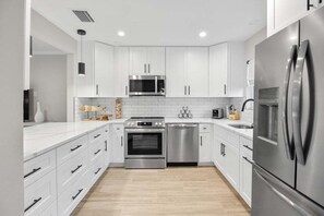 A modern kitchen with white cabinets, stainless steel appliances, and a wooden floor. - Seashells Unit 18-coastal Breeze 2 Bedroom Condo (Sanibel)