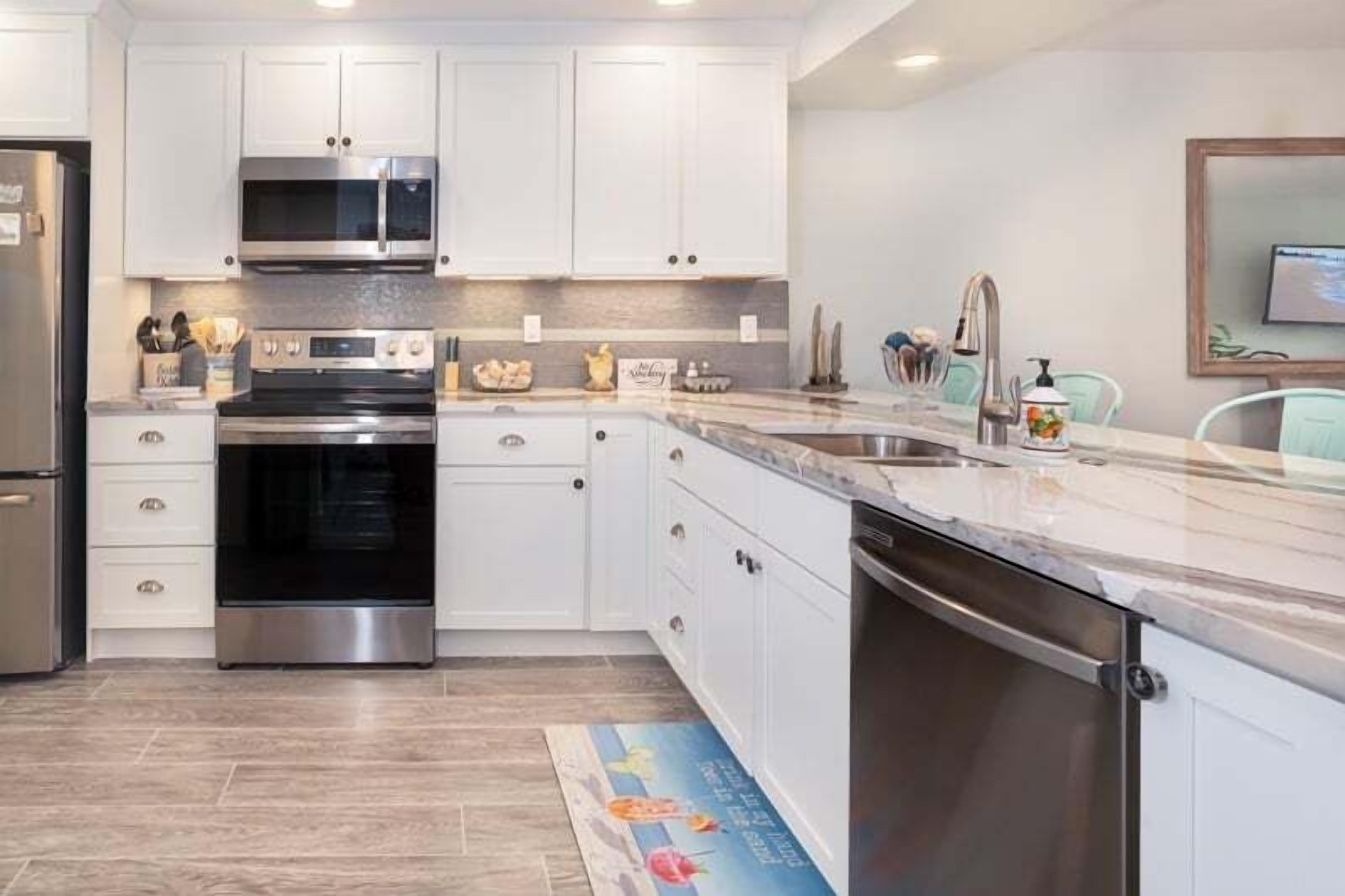 A modern kitchen with white cabinets, stainless steel appliances, and a marble countertop.