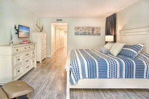 A bedroom with a bed, a dresser, a chair, and a painting on the wall. - Lighthouse Point 222 3 Bedroom Condo (Sanibel)
