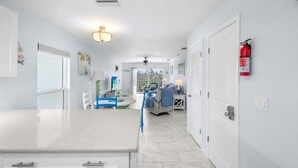 A modern kitchen with white cabinetry, a marble countertop, and a dining area with a blue chair and table. - Seashells Unit 44 2 Bedroom Condo (Sanibel)
