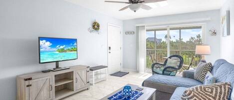 A living room with a television, a ceiling fan, a sofa, and a view of the outdoors through a sliding glass door.