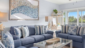 A living room with two sofas, a glass coffee table, and a large abstract painting. - Seashells Unit 12 2 Bedroom Condo (Sanibel)