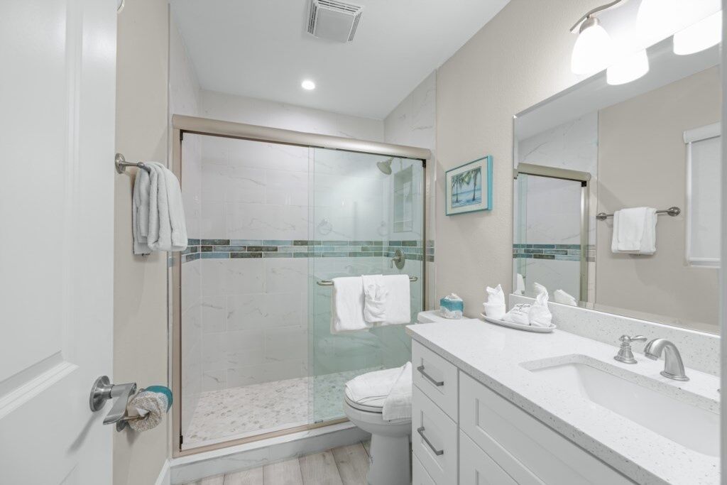 Un baño moderno con ducha envuelta en vidrio, inodoro blanco y tocador con lavamanos y espejo.