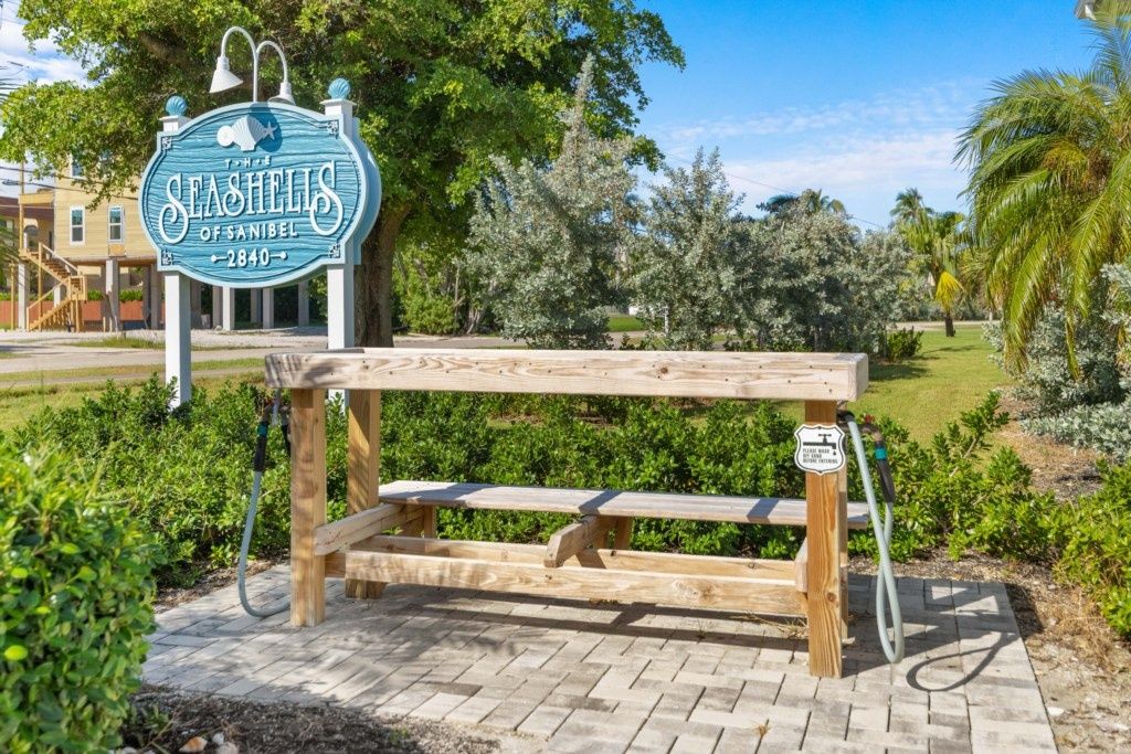 Un banc en bois avec une pancarte indiquant « Les coquillages de Sanibel » et une maison de plage en arrière-plan.