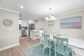 Een moderne keuken met witte kasten, een roestvrijstalen koelkast en een eethoek met een witte tafel en blauwe stoelen.