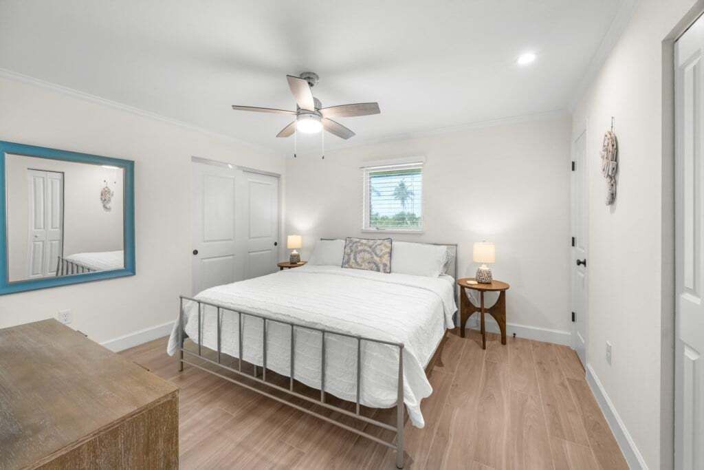 Une chambre à coucher avec un lit, un ventilateur de plafond, une fenêtre et une table de chevet avec une lampe.