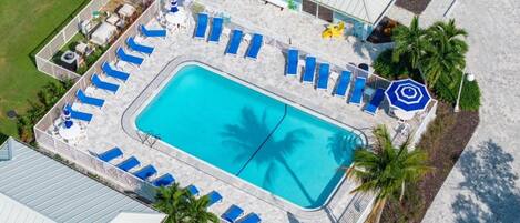 Oversigtsbillede af et resort med swimmingpool, liggestole og palmer.