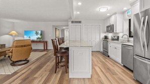A modern kitchen with white cabinets, stainless steel appliances, and a wooden dining area. - Kings Crown Unit 212 2 Bedroom Condo (Sanibel)