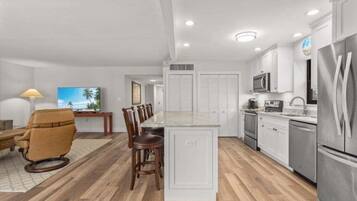 A modern kitchen with white cabinets, stainless steel appliances, and a wooden dining area.
