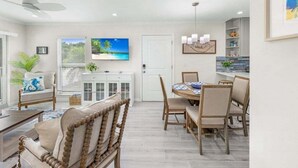 A spacious living area with a dining table, comfortable seating, a television, and a view of the outdoors. - Seashells Unit 33 2 Bedroom Condo (Sanibel)