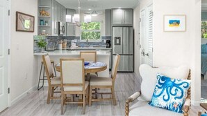 A modern kitchen with grey cabinets, a stainless steel refrigerator, and a dining area with wooden chairs and a table. - Seashells Unit 33 2 Bedroom Condo (Sanibel)