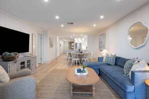 Ein modernes Wohnzimmer mit Sofa, Couchtisch und Fernseher. Es gibt einen Essbereich mit Stühlen und Tisch.