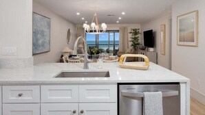 A modern kitchen with a central island, a built-in dishwasher, and a view of the ocean. - Sanddollar A302 3 Bedroom Condo (Sanibel)