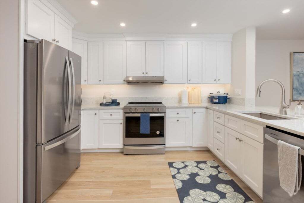A modern kitchen with white cabinets, stainless steel appliances, and a patterned rug.