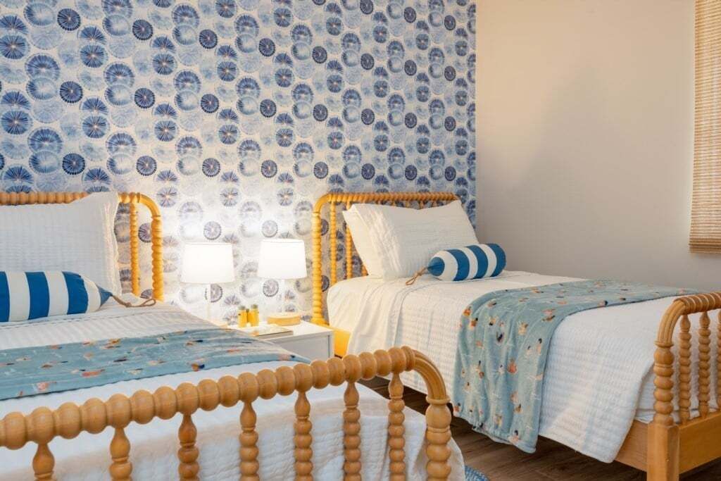 A bedroom with two wooden beds, a patterned wallpaper, and a nightstand with a lamp.