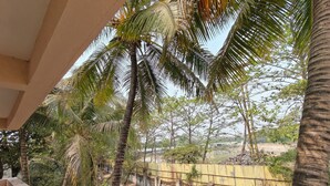 A balcony with a view of palm trees and a fenced area with construction materials. - Beautiful 1-bedroom bungalow in pleasant Pune neighborhood (Pune)