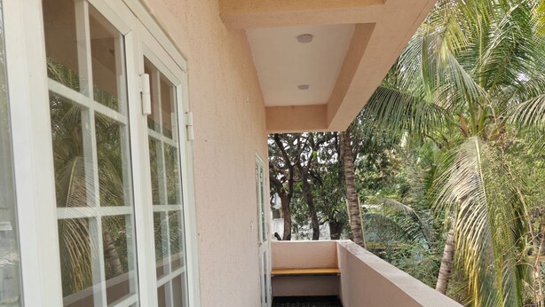A narrow corridor with patterned floor tiles, a white door, and a view of palm trees outside. - Beautiful 1-bedroom bungalow in pleasant Pune neighborhood (Pune)