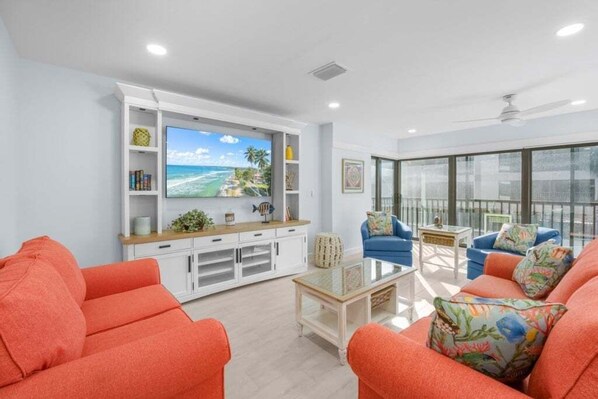 Ein modernes Wohnzimmer mit Flachbildfernseher, orangefarbenen Sofas, einem Couchtisch und einem Balkon mit Blick.