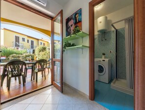 A room with a sliding glass door leading to an outdoor area with a table and chairs. There is a washing machine and a shower in the room. - Comfortable Accommodation With Patio (Badesi)