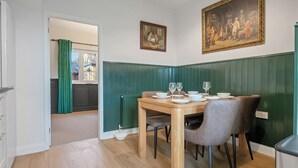 A dining area with a wooden table set for four, green paneled walls, and a painting above the table.
