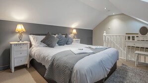 A bedroom with a bed, nightstands, a dresser, and a staircase.