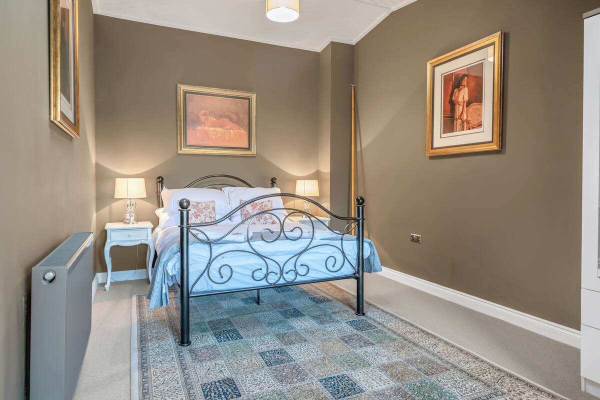 A bedroom with a bed, bedside tables, a radiator, and a patterned rug.