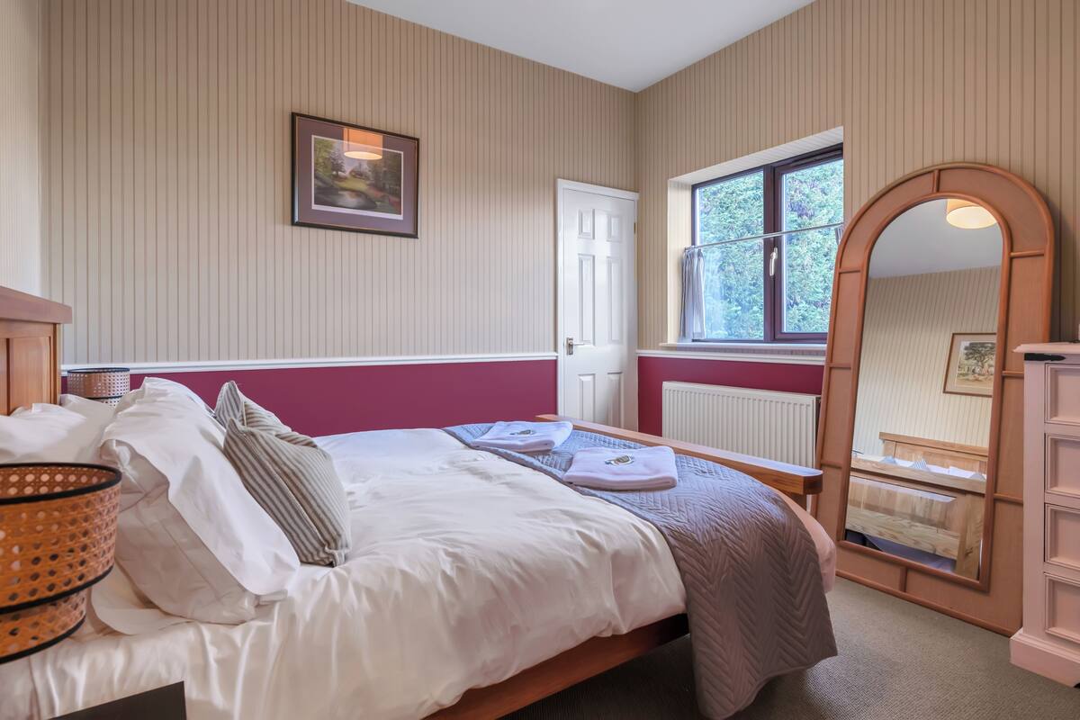 A bedroom with a bed, a window, a mirror, and a door.